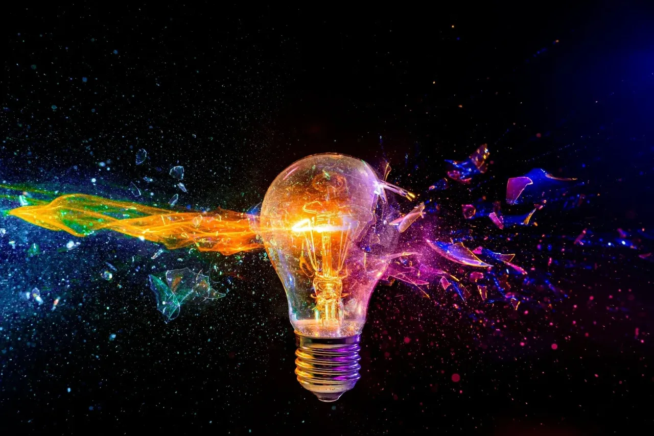 A glowing light bulb bursting apart in streaks of orange, blue and purple light against a black background.